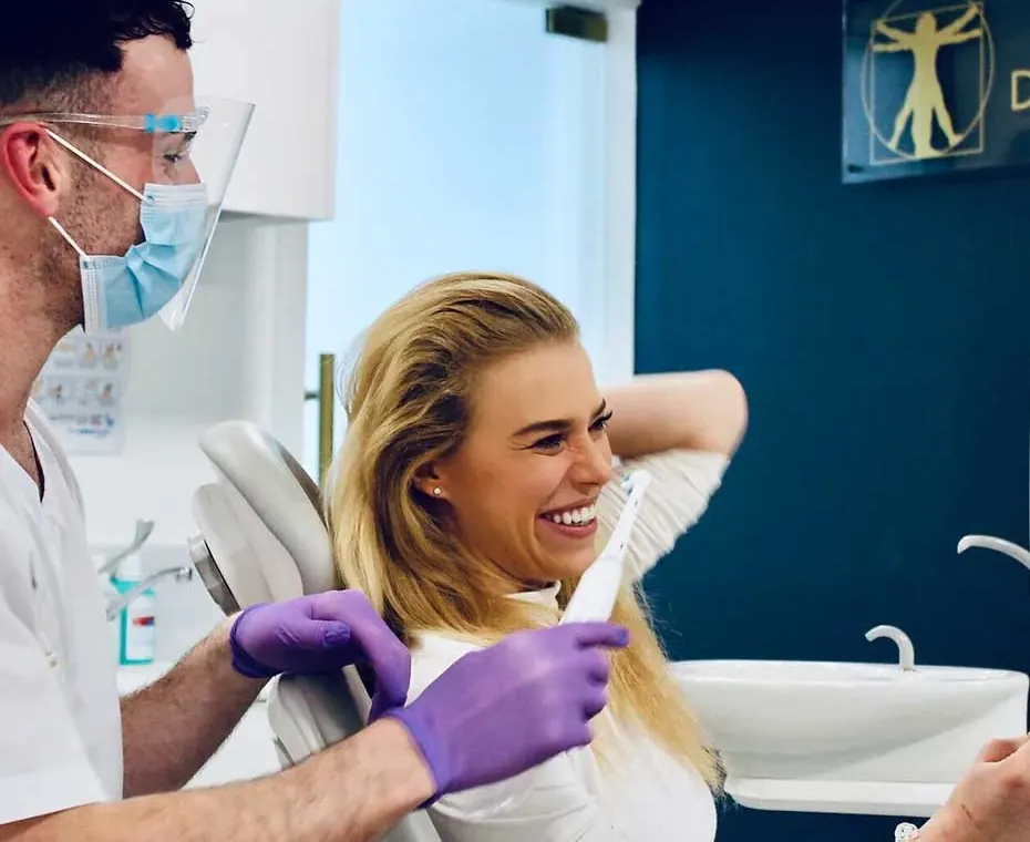 A patient laughing with her dentist who is holding a tooth brush